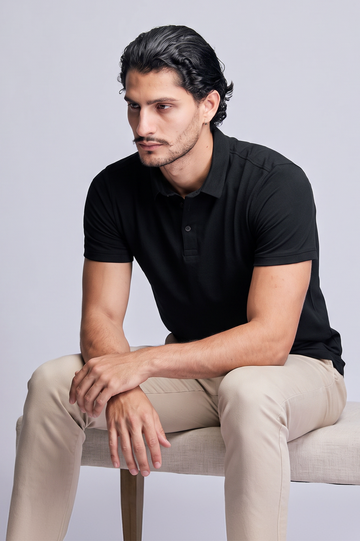 Homem sentado vestindo PoloTech preta e calça chino, fundo cinza de estúdio